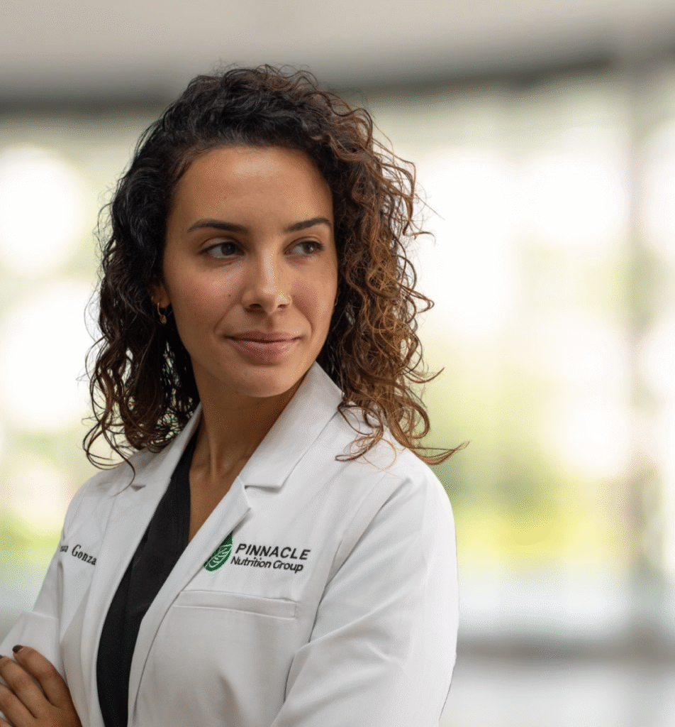 Vanessa Gonzalez, registered dietitian at Pinnacle Nutrition Group, wearing a white lab coat, confidently standing in a wellness clinic environment