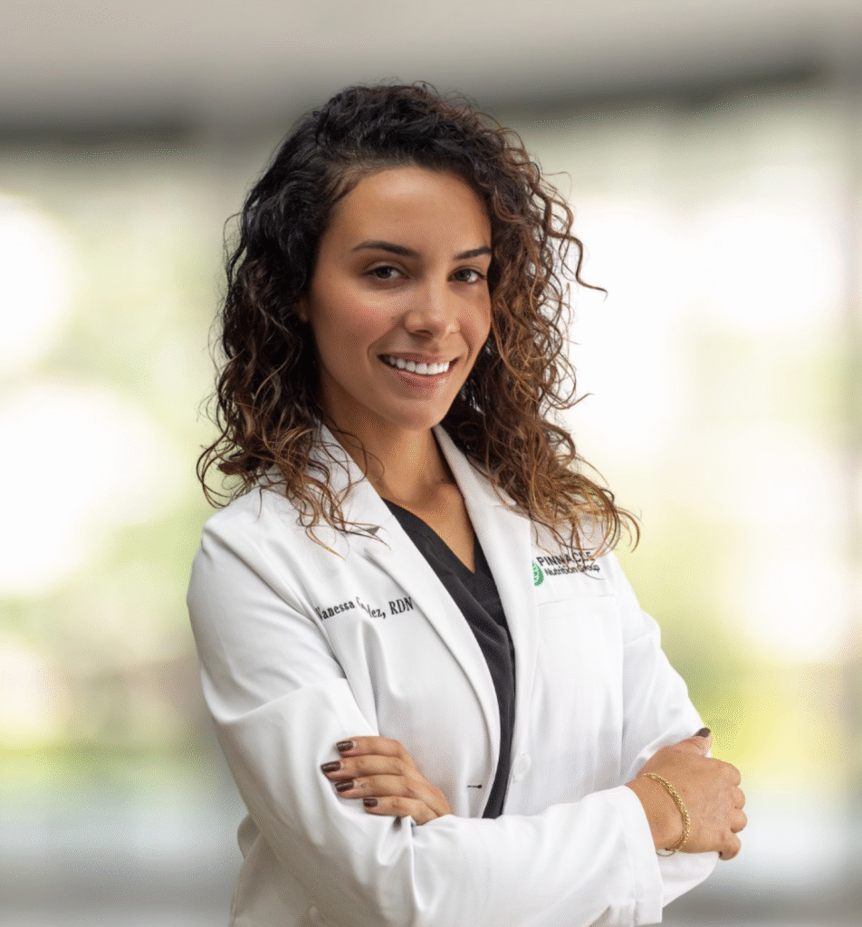 Vanessa Gonzalez, registered dietitian at Pinnacle Nutrition Group, wearing a white lab coat, confidently standing in a wellness clinic environment